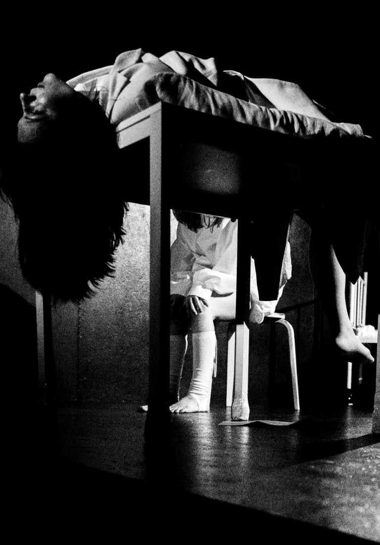 A figure lies across a table, head fallen back