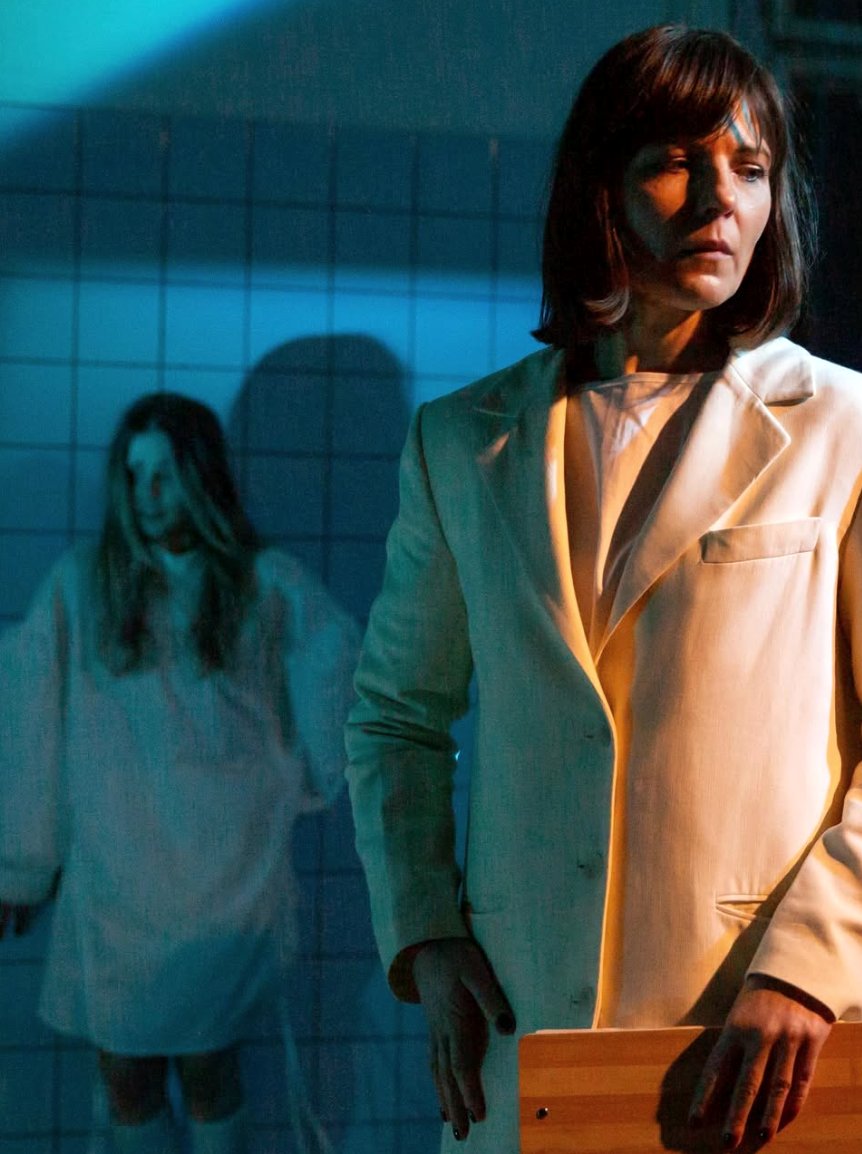 A woman in a pale suit; a ghost in the background